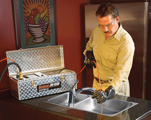 Drain cleaning technician de-clogging a blocked kitchen sink. 